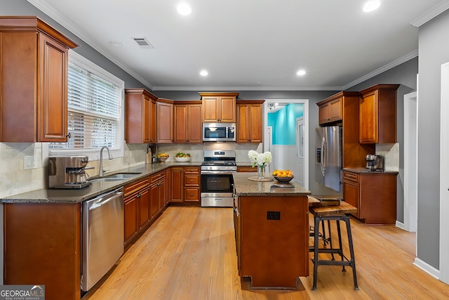 kitchen with a kitchen breakfast bar, sink, light hardwood / wood-style floors, appliances with stainless steel finishes, and a kitchen island