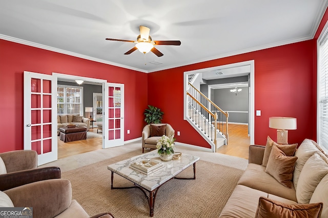 living room featuring ceiling fan with notable chandelier, light wood-type flooring, ornamental molding, and french doors