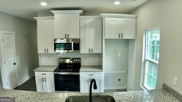 kitchen with appliances with stainless steel finishes, dark wood-type flooring, decorative backsplash, light stone counters, and white cabinets