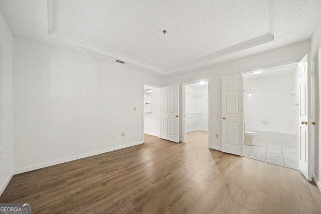 unfurnished bedroom featuring ensuite bathroom, a tray ceiling, a spacious closet, a closet, and hardwood / wood-style flooring