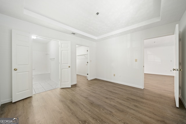 unfurnished bedroom with a closet, a raised ceiling, hardwood / wood-style floors, and a walk in closet