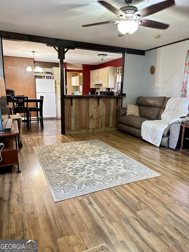 living room with hardwood / wood-style flooring, ceiling fan with notable chandelier, and a textured ceiling