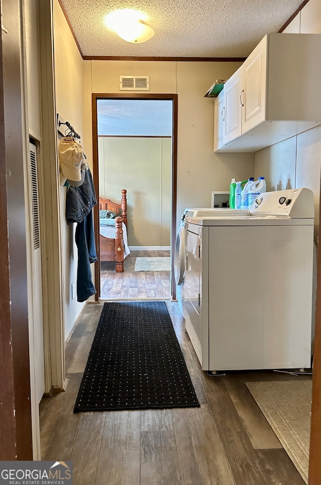 clothes washing area featuring hardwood / wood-style floors, cabinets, a textured ceiling, and independent washer and dryer