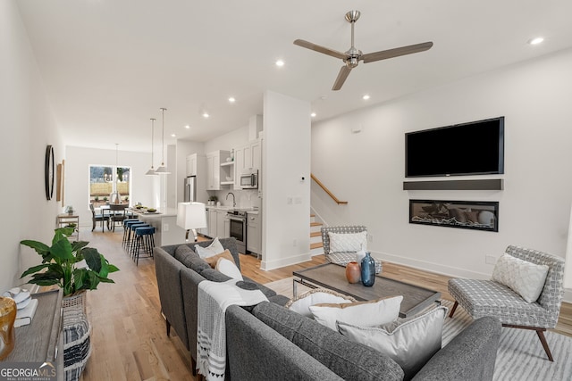 living room featuring light wood-type flooring, ceiling fan, and sink