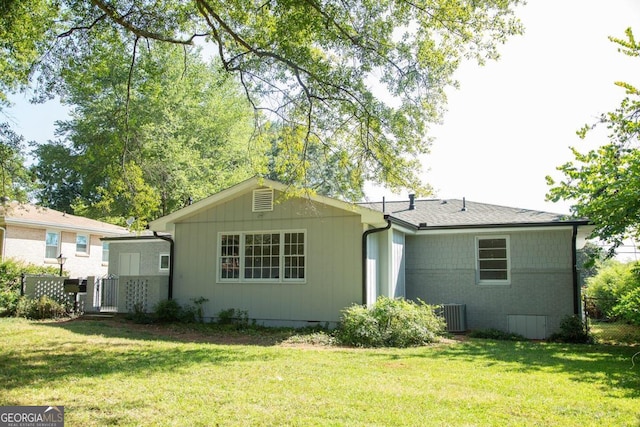 rear view of property with central AC unit and a lawn