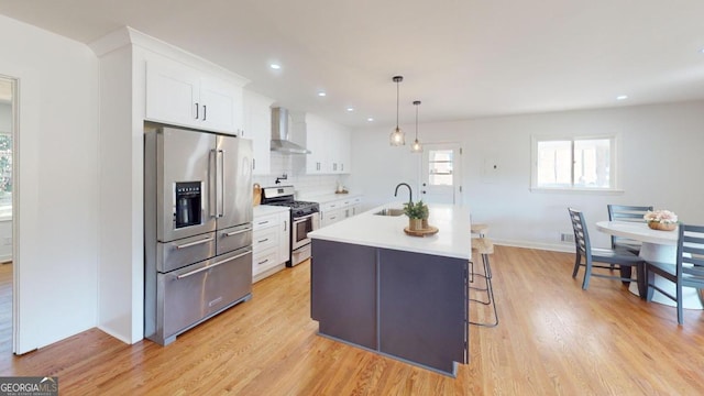 kitchen with tasteful backsplash, stainless steel appliances, white cabinetry, wall chimney range hood, and light wood-type flooring