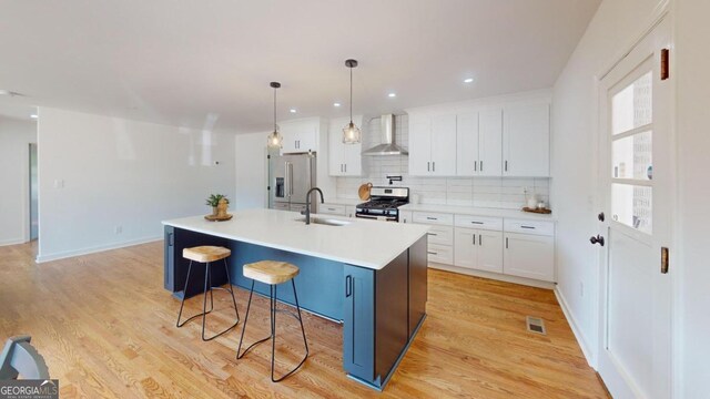 kitchen featuring light hardwood / wood-style floors, a kitchen island with sink, stainless steel appliances, wall chimney range hood, and white cabinets