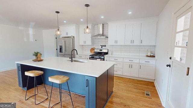 kitchen with light hardwood / wood-style flooring, sink, wall chimney exhaust hood, appliances with stainless steel finishes, and a center island with sink