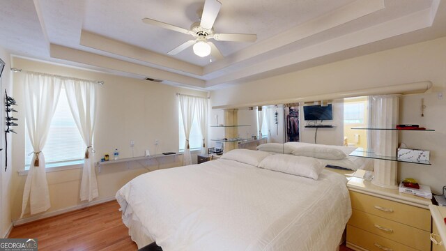 bedroom featuring a raised ceiling, light hardwood / wood-style flooring, and ceiling fan