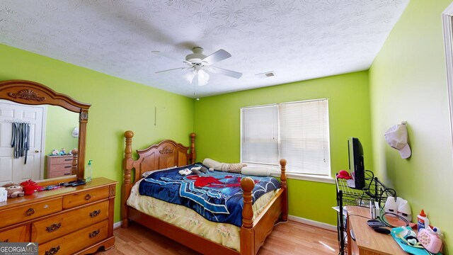 bedroom with light wood-type flooring, ceiling fan, and a textured ceiling