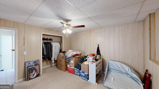 interior space featuring ceiling fan, wood walls, a closet, and a drop ceiling