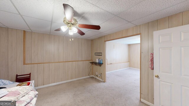 living area with a paneled ceiling, ceiling fan, carpet floors, and wooden walls