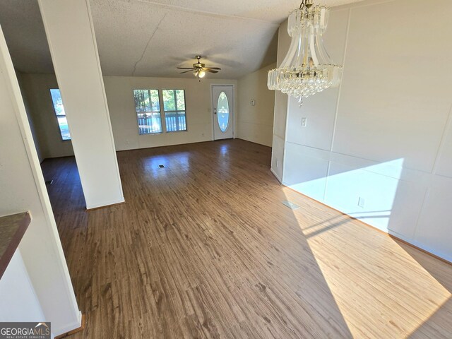 empty room with a textured ceiling, ceiling fan with notable chandelier, vaulted ceiling, and wood-type flooring