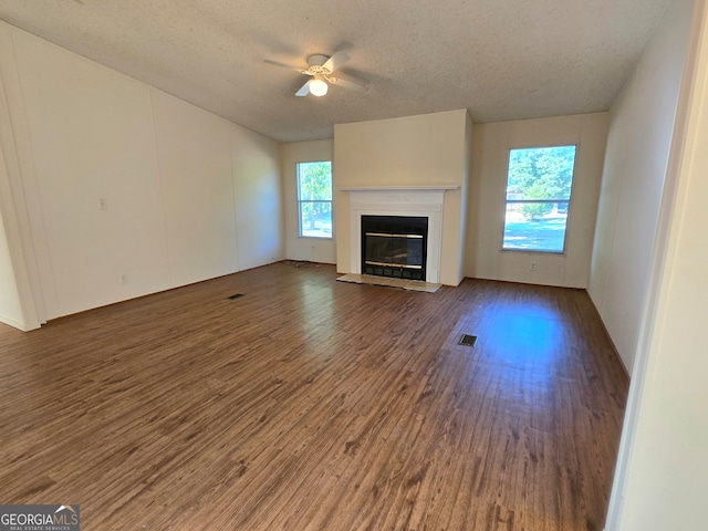 unfurnished living room with ceiling fan, a textured ceiling, dark wood-type flooring, and a healthy amount of sunlight