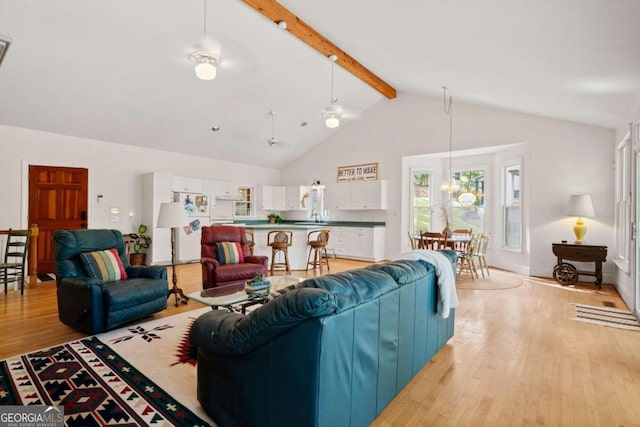 living room featuring ceiling fan with notable chandelier, beam ceiling, light wood-type flooring, and high vaulted ceiling