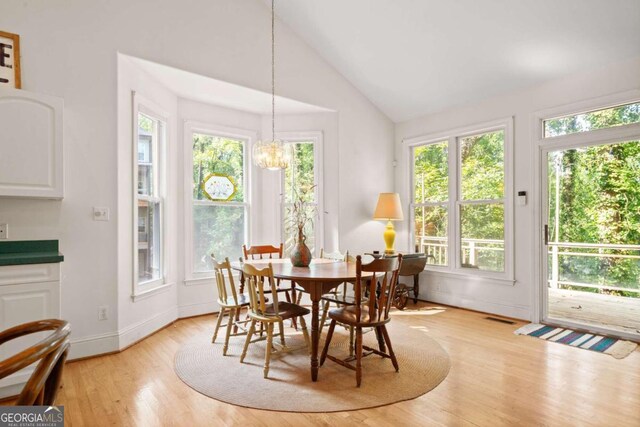 dining room featuring a chandelier, high vaulted ceiling, light hardwood / wood-style floors, and a healthy amount of sunlight