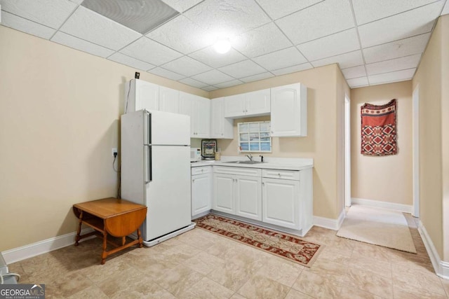 kitchen with a paneled ceiling, sink, white fridge, and white cabinets