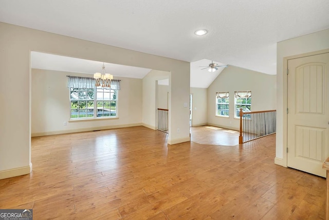 interior space featuring vaulted ceiling, ceiling fan with notable chandelier, light wood-type flooring, and baseboards