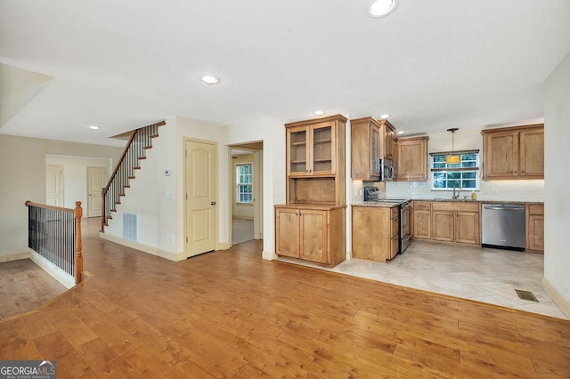 kitchen featuring visible vents, brown cabinetry, light wood-style flooring, stainless steel appliances, and a sink