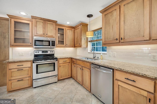 kitchen with pendant lighting, stainless steel appliances, backsplash, a sink, and light stone countertops