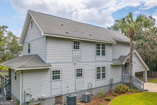 rear view of house with cooling unit and roof with shingles