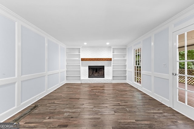 unfurnished living room with built in shelves, a brick fireplace, a decorative wall, and dark wood-style flooring