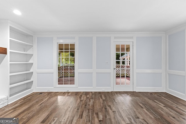 empty room with ornamental molding, wood finished floors, built in features, and a decorative wall