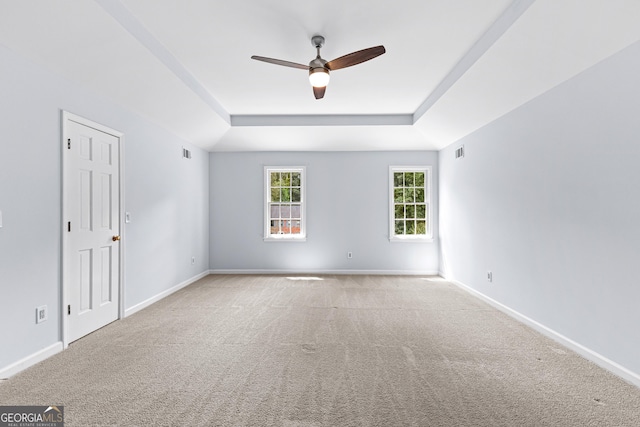 empty room with a tray ceiling, visible vents, carpet flooring, ceiling fan, and baseboards