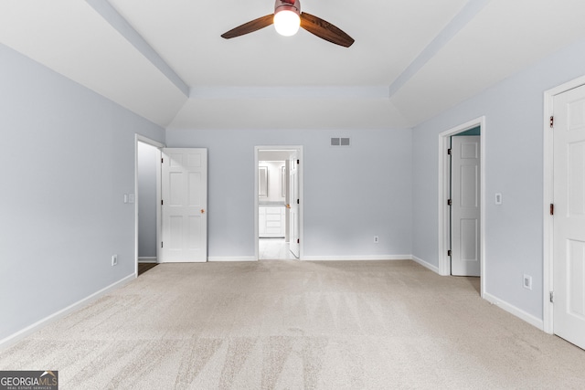 unfurnished bedroom featuring light carpet, baseboards, visible vents, a raised ceiling, and ensuite bathroom