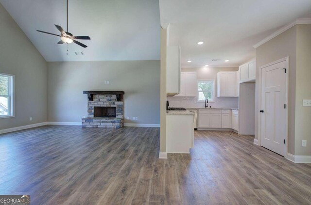 unfurnished living room featuring high vaulted ceiling, wood-type flooring, sink, ceiling fan, and a stone fireplace