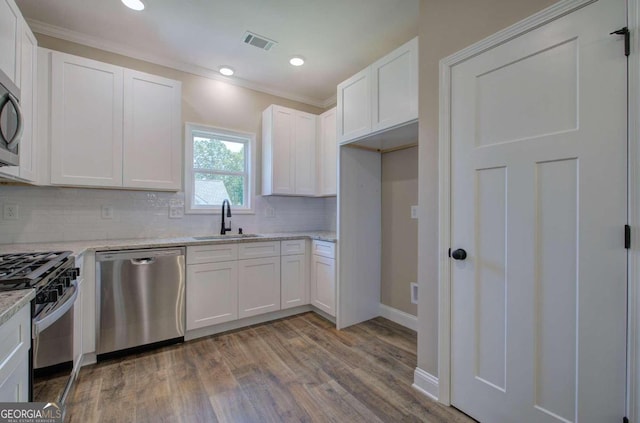 kitchen featuring light wood-type flooring, ornamental molding, sink, decorative backsplash, and appliances with stainless steel finishes