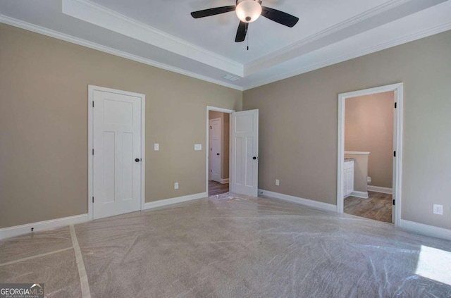 unfurnished bedroom featuring light carpet, ornamental molding, ensuite bath, ceiling fan, and a tray ceiling