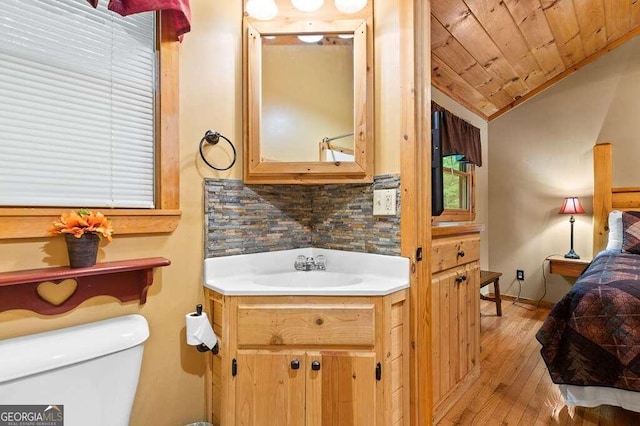 bathroom with vaulted ceiling, toilet, wood-type flooring, decorative backsplash, and vanity