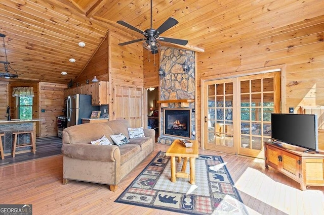 living room featuring wood walls, a fireplace, wood ceiling, ceiling fan, and light wood-type flooring