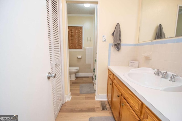 bathroom with toilet, ornamental molding, vanity, wood-type flooring, and tile walls