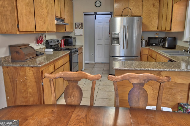 kitchen with stainless steel appliances, sink, kitchen peninsula, a barn door, and light tile patterned flooring