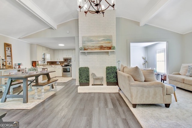 living room featuring a chandelier, a brick fireplace, ornamental molding, light hardwood / wood-style floors, and lofted ceiling with beams