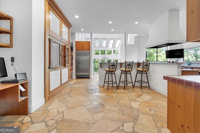 kitchen with custom range hood, kitchen peninsula, stainless steel built in refrigerator, and a kitchen breakfast bar