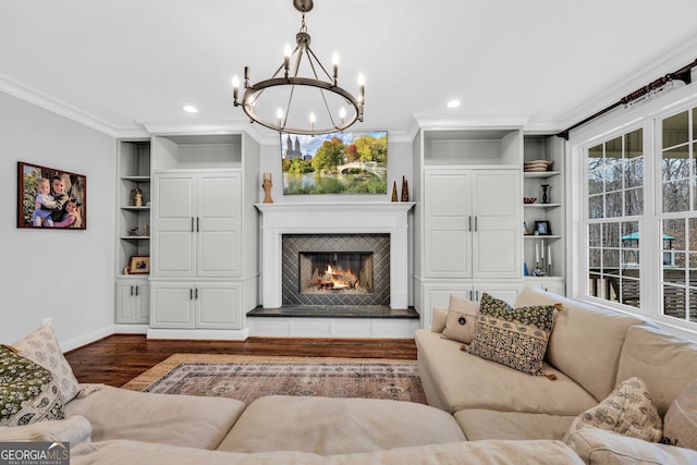 living room featuring hardwood / wood-style flooring, a tiled fireplace, crown molding, a chandelier, and built in features