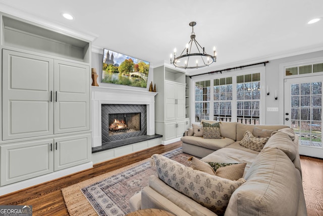 living room featuring hardwood / wood-style floors, a tiled fireplace, a notable chandelier, and ornamental molding