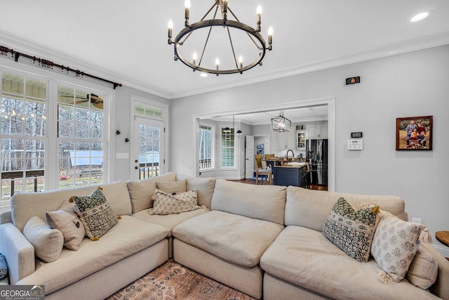 living room featuring an inviting chandelier, crown molding, and a healthy amount of sunlight