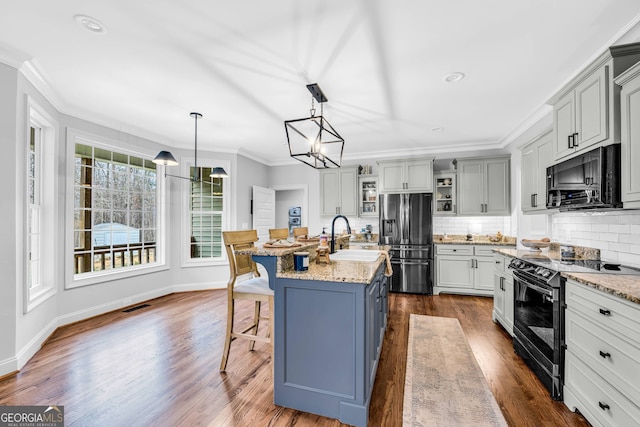 kitchen featuring black appliances, sink, an island with sink, decorative backsplash, and dark wood-type flooring