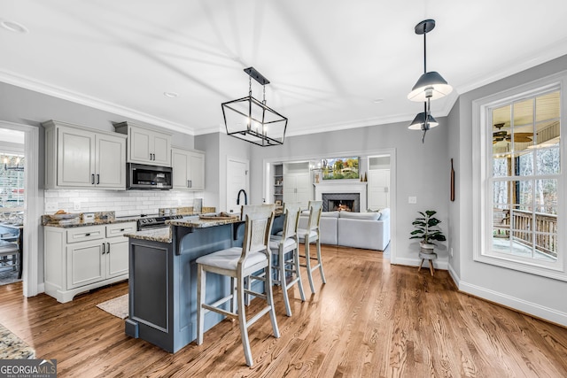 kitchen featuring gray cabinetry, stainless steel appliances, light hardwood / wood-style floors, dark stone counters, and a kitchen bar