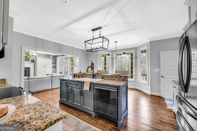 kitchen with gray cabinetry, hardwood / wood-style floors, a kitchen island with sink, crown molding, and sink