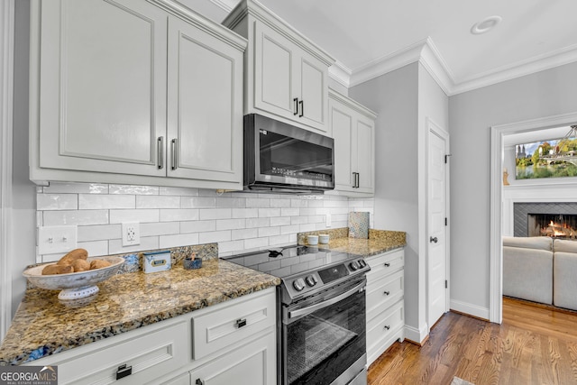 kitchen with hardwood / wood-style floors, tasteful backsplash, stainless steel appliances, ornamental molding, and dark stone countertops