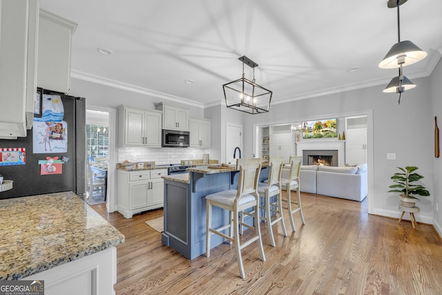 kitchen featuring a kitchen island with sink, tasteful backsplash, light hardwood / wood-style floors, stainless steel appliances, and light stone counters