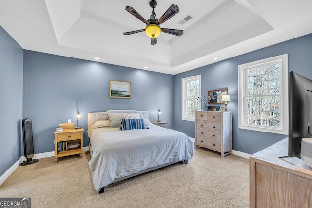 bedroom with a tray ceiling, multiple windows, and light carpet