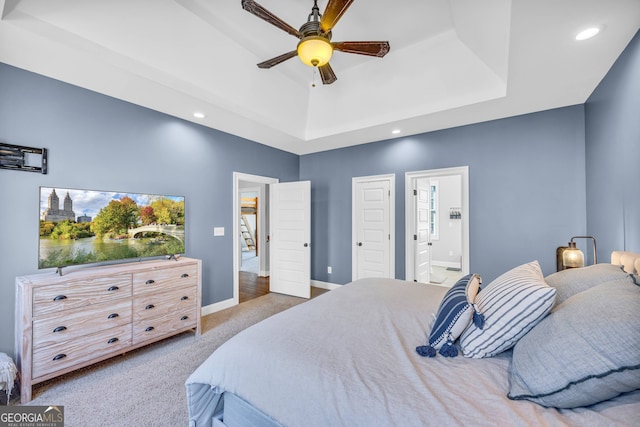 bedroom with a tray ceiling, connected bathroom, ceiling fan, and carpet floors