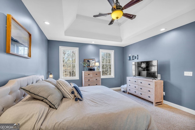 bedroom with a raised ceiling, ceiling fan, and light colored carpet