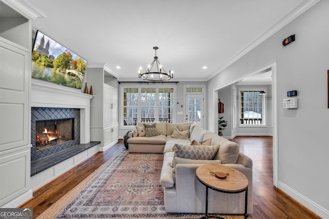 living room with dark wood-type flooring, ornamental molding, a tile fireplace, and a notable chandelier